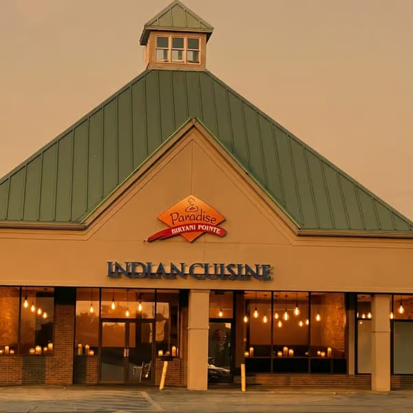 Exterior of Paradise Biryani Pointe, an Indian cuisine restaurant, with a green roof and warm window lights.