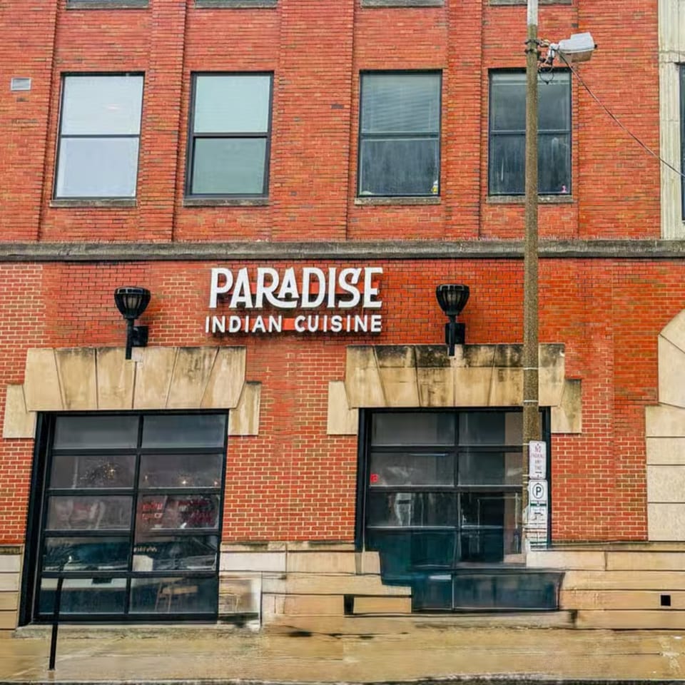 Exterior of Paradise Indian Cuisine, a red brick building with large windows and a street lamp.