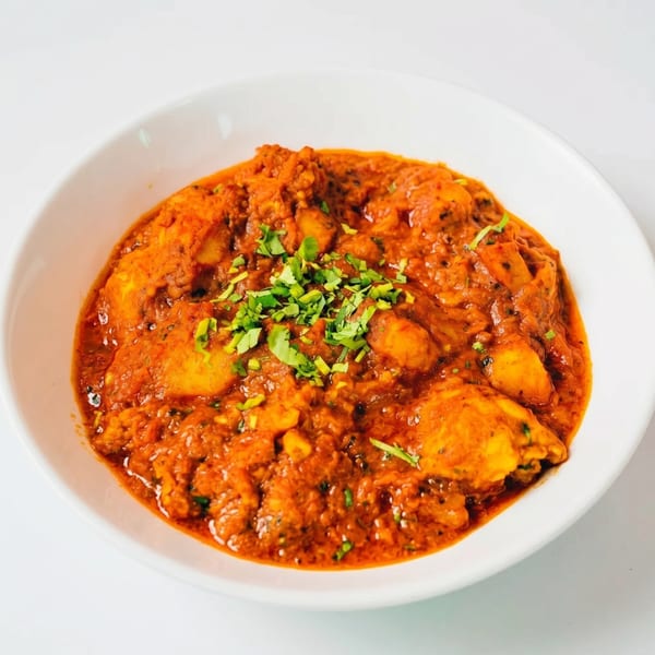 A white bowl filled with a rich, orange-red curry, garnished with fresh green herbs.
