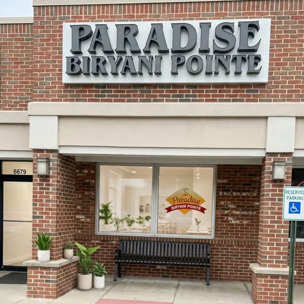 Exterior of Paradise Biryani Pointe, a brick building with a large sign and a bench outside.