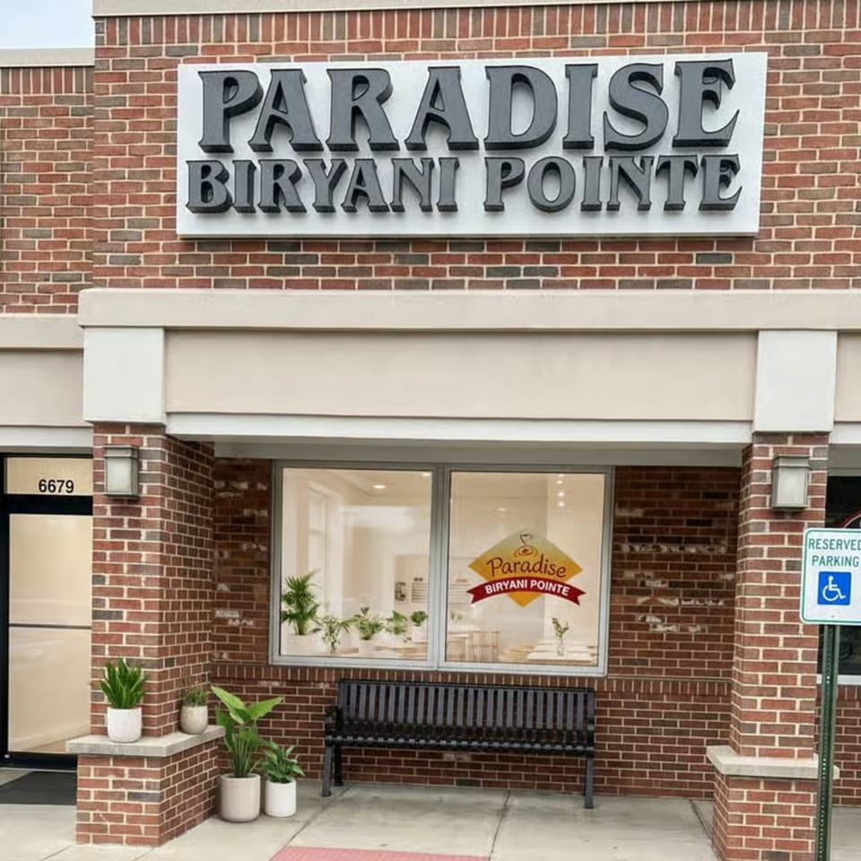 Exterior of Paradise Biryani Pointe, a brick building with a large sign and a bench outside.