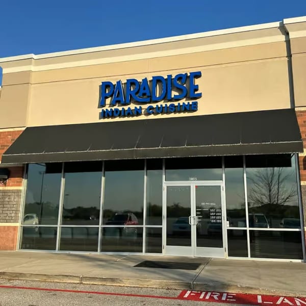 Exterior of Paradise Indian Cuisine restaurant with a black awning and large glass windows.