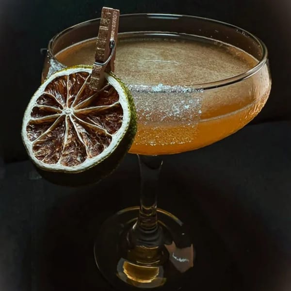 A golden cocktail in a coupe glass, garnished with a dried lime slice and sugar rim.